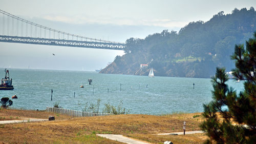 Scenic view of suspension bridge over sea against sky