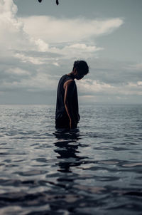 Rear view of man standing in sea against sky during sunset