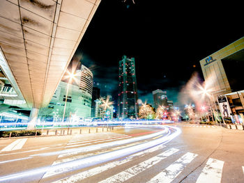 Light trails on road amidst buildings against sky at night