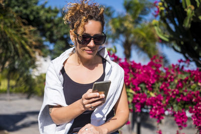 Mid adult woman using mobile phone against trees