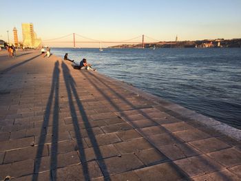 People on suspension bridge over sea against clear sky