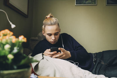 Male teenager using smart phone while resting on bed at home