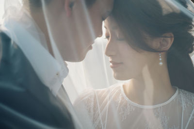 Close-up of romantic newlywed couple under veil