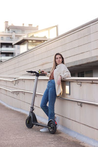 Vertical view of young woman leaning resting with her electric scooter wating for her friend to come