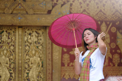 Woman holding pink umbrella while standing against historic building