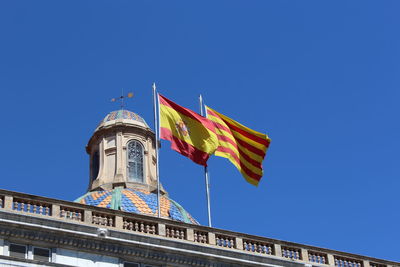 Low angle view of palau de la generalitat de catalunya with spanish and catalonia flags against clear blue sky