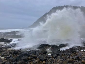 Scenic view of waves breaking on rocks against sky