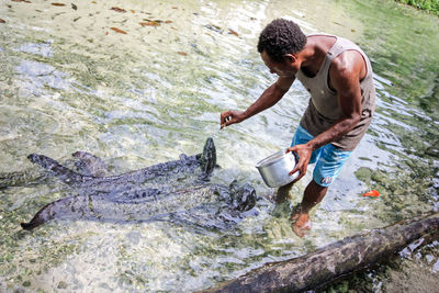 Side view of shirtless man with fish in river