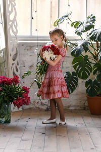 Cute girl with bouquet standing amidst potted plants on floor at home
