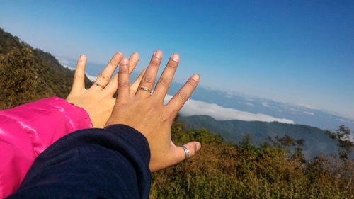 Cropped hands of couple showing rings against sky