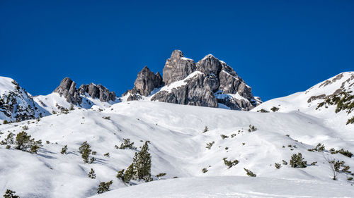 Low angle view of snowcapped mountains against clear blue sky