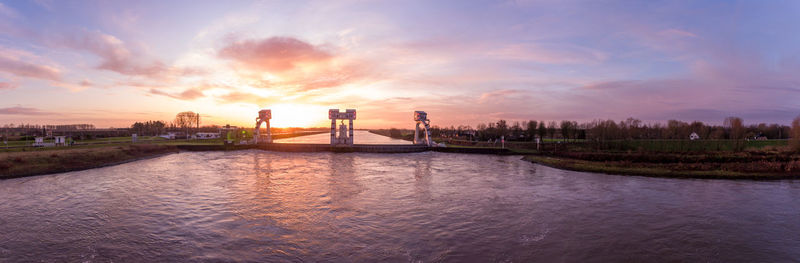 Scenic view of river by buildings against sky during sunset