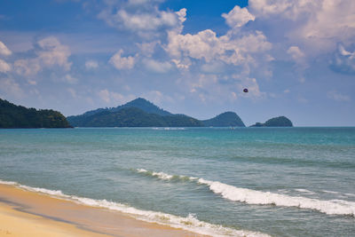 Waves of the azure andaman sea under the blue sky reaching the shores of cenang beach