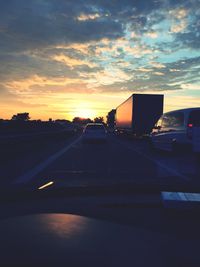 Cars on road against cloudy sky at sunset