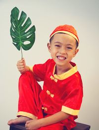 Portrait of smiling boy holding red leaf against white background