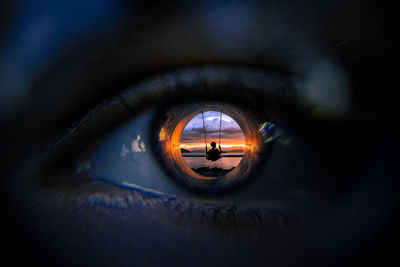 Digitally generated image of boy swinging at beach reflecting on man eyeball