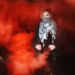 Portrait of young woman wearing scarf while standing amidst red smoke