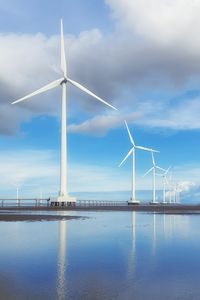 Wind turbines by sea against sky