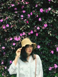 Beautiful young woman standing against pink flowering plants