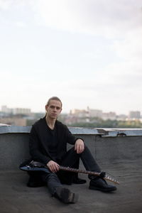 Full length portrait of young man with guitar sitting on building terrace