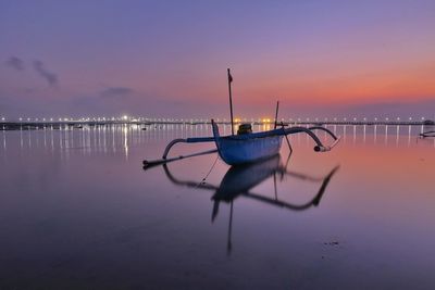 Outrigger boat at beach against sky during sunset