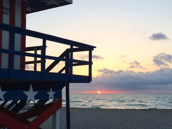 Lifeguard on beach by sea against sky during sunset