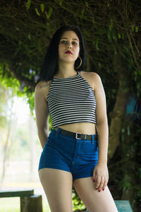 Portrait of beautiful young woman standing against trees