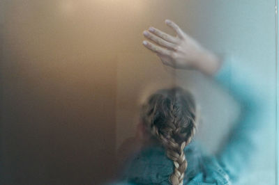 Rear view of woman with braided hair seen through wet glass