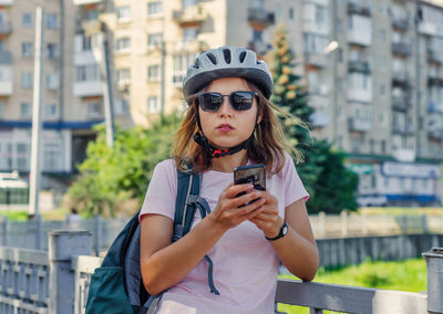 Girl in black glasses and a bicycle helmet uses a smartphone on the street