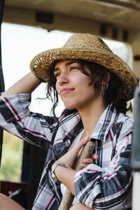 Smiling woman wearing hat looking away while sitting outdoors