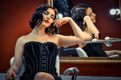 Beautiful woman wearing corset sitting with eyes closed by mirror