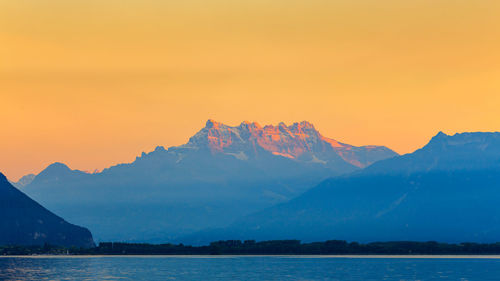 Scenic view of sea and mountains against orange sky