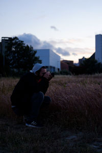 Side view of man sitting on field against sky