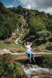 Woman sitting by plants against trees