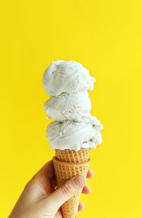 Hand holding ice cream cone against yellow background