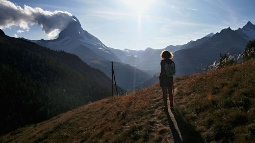 Rear view of hiker standing on mountain against sky