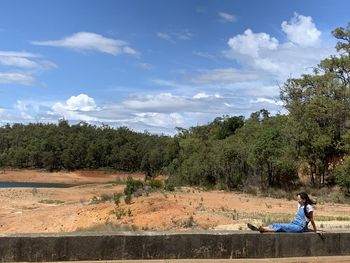 Side view of man sitting on land against sky