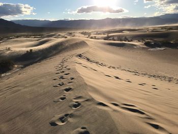 Footprints on sand dune in desert against sky