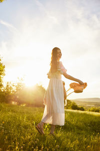 Side view of woman standing on field against sky during sunset