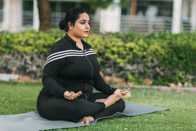 An indian woman practices yoga and meditation in the lotus asana pose in an outdoor summer park. 