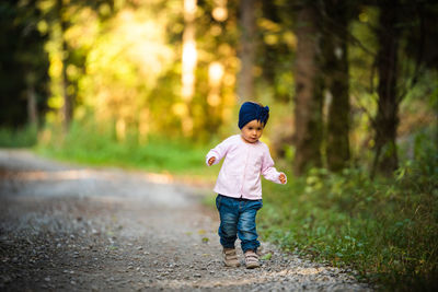 Full length of baby girl walking on dirt road amidst forest