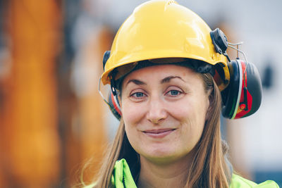 Portrait of smiling female worker wearing hardhat and ear muffs