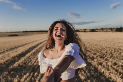 Smiling young woman standing on field against sky