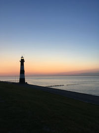 Lighthouse by sea against sky during sunset