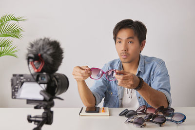 Portrait of boy holding camera while sitting on table