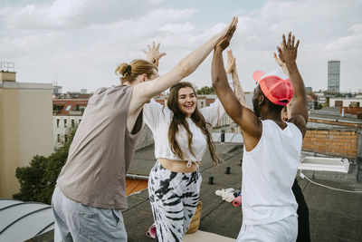 Happy multiracial male and female friends with arms raised giving high-five to each other on rooftop