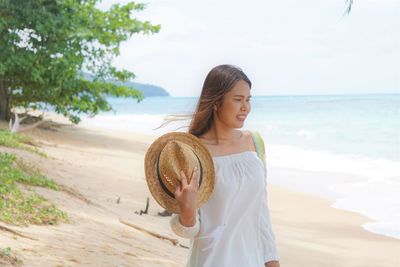 Young woman standing at beach against sky