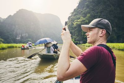 Side view of man photographing in boat against mountains