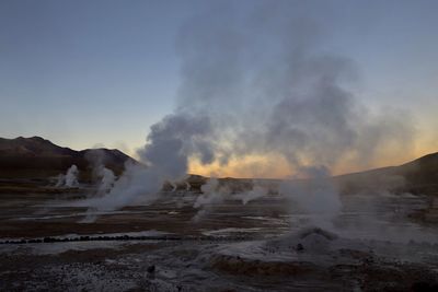 Smoke emitting from volcanic landscape against clear sky during sunset