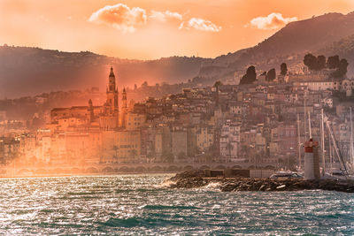 Cityscape by sea against sky during sunset